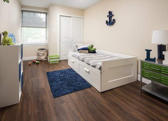 A bedroom with a white bed, a blue rug, and a green drawer.
