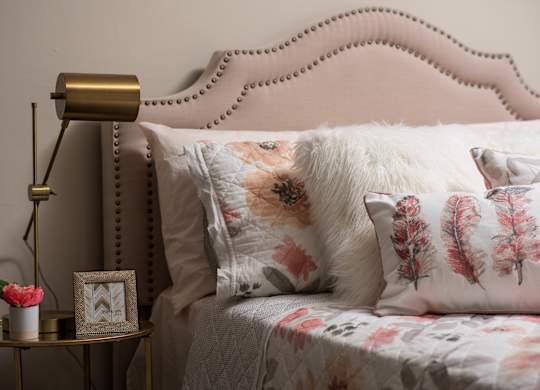 A bed with a pink headboard and floral pillows is shown.