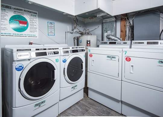 A row of white front load washing machines are lined up in a laundry room.