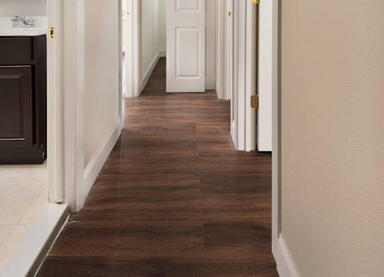 A long hallway with white doors and brown floors.