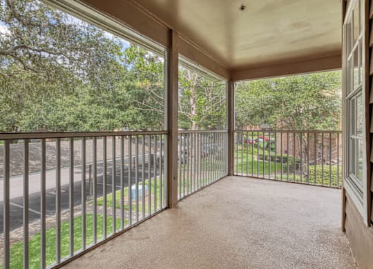 A balcony with a metal railing and a view of a street and trees.