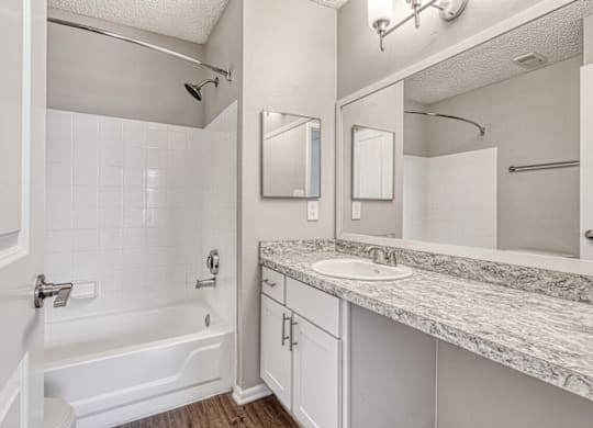 A white bathroom with a marble counter top and a white tub.