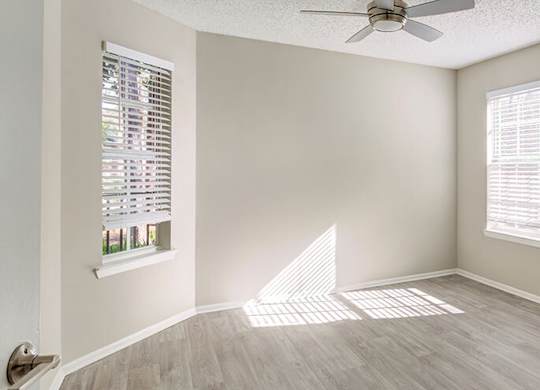 A room with a ceiling fan and two windows.