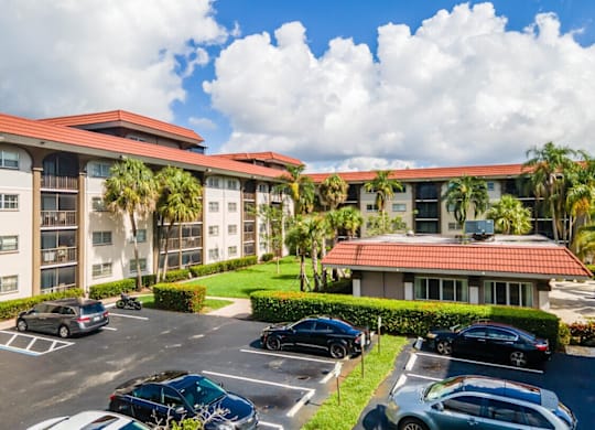 A parking lot with cars and a building with palm trees in front.