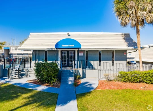 the front of a building with a blue roof and a porch with a palm tree  at The Park at Chesterfield Apartment Homes, Tampa, Florida