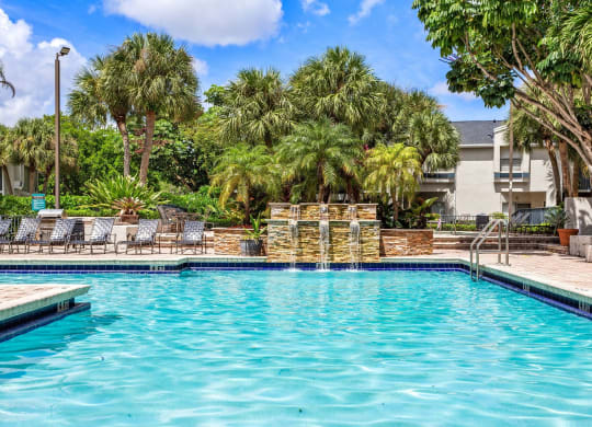a swimming pool with palm trees and a building in the background at Waterford Park Apartment Homes, LLC, Lauderhill, FL