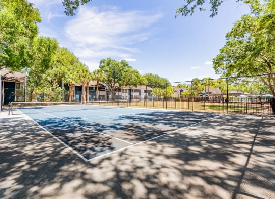 a tennis court with trees and a fence around it  at Fisherman's Landing Apartment Homes, Tampa, Florida