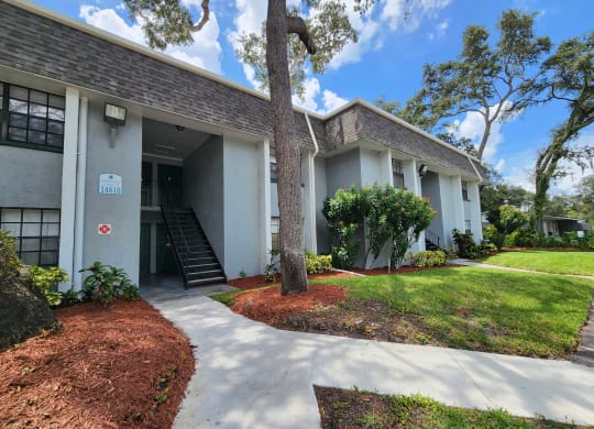 the front of a white building with a sidewalk and trees at Greenwich Commons Apartment Homes, Tampa, FL