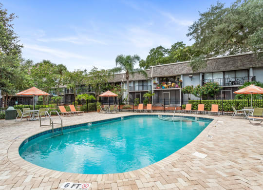 a resort style pool with chairs and umbrellas in front of a building at Greenwich Commons Apartment Homes, Tampa, 33613