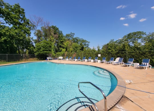 a swimming pool with chairs and trees in the background at Raritan Crossing Apartment Homes, New Brunswick, 08901
