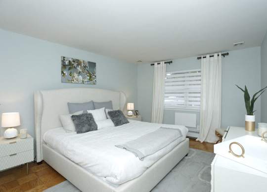 A white bedroom with a large bed and a nightstand with a plant on it.
