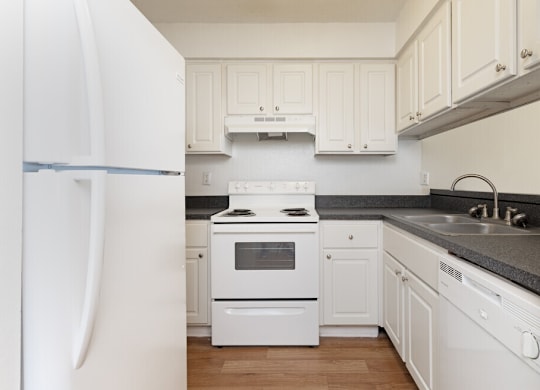 A white kitchen with a refrigerator, stove, and cabinets.