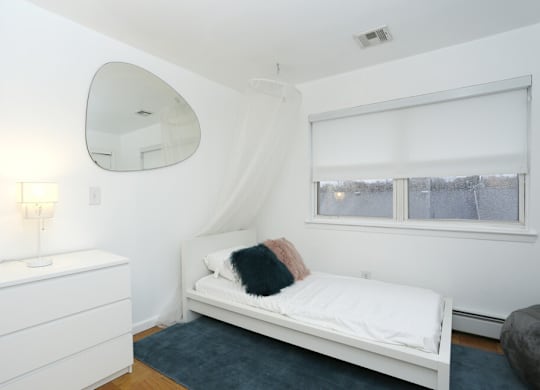 A white bedroom with a bed, dresser, and mirror.