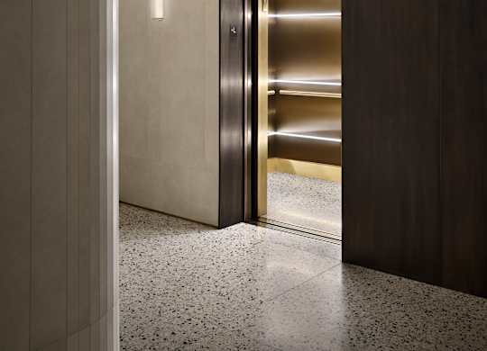 A modern elevator with a closed door is located in a hallway with a speckled floor.