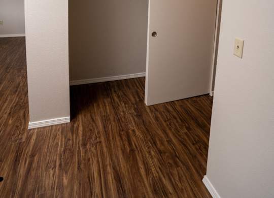 A white door is open to a room with wood flooring.