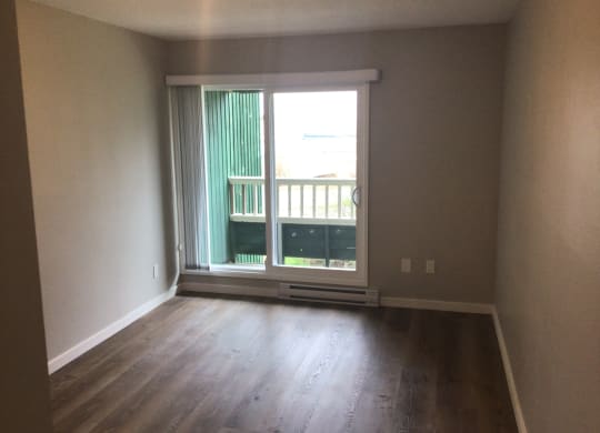 an empty living room with a large window and wooden floors