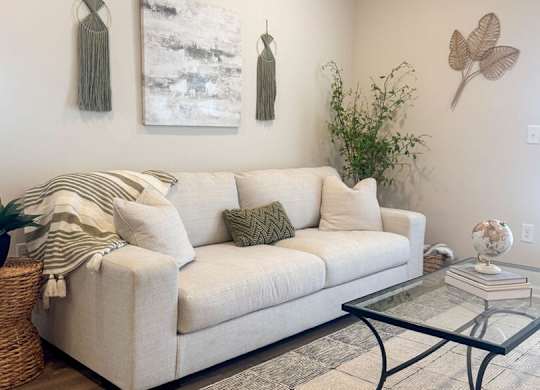 A living room with a white couch, a glass coffee table, and two wall hangings.