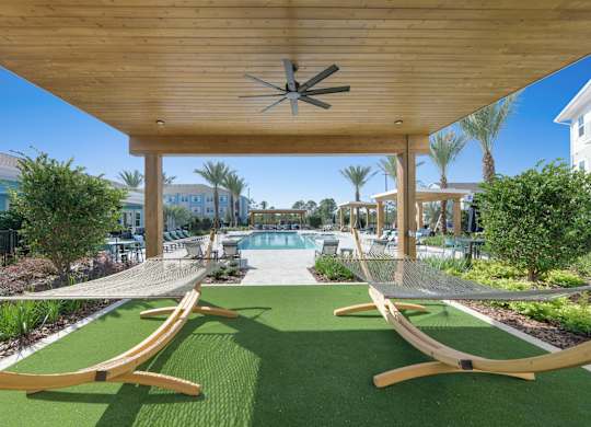 A wooden pergola with a ceiling fan is over a green lawn with two hammocks.at Allegra at Cocoa in Cocoa, FL, 32926