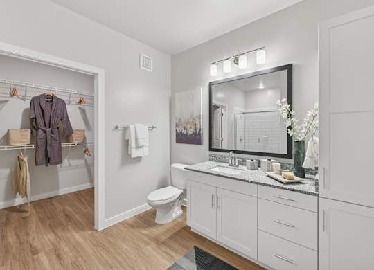 A bathroom with a toilet, sink, mirror, and wooden floors.at Allegra at Cocoa in Cocoa, FL, 32926