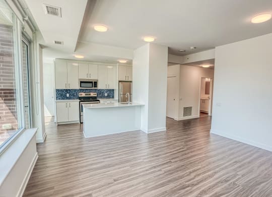 an empty living room and kitchen with white cabinets and wood flooring