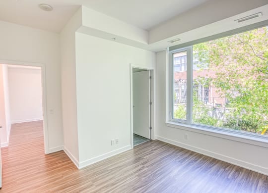 an empty living room with a large window and wood flooring