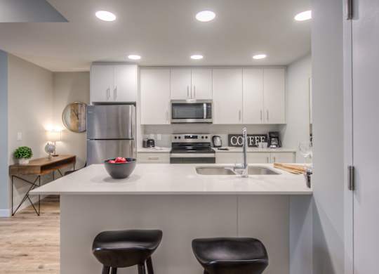 a kitchen with white cabinets and a counter with two stools