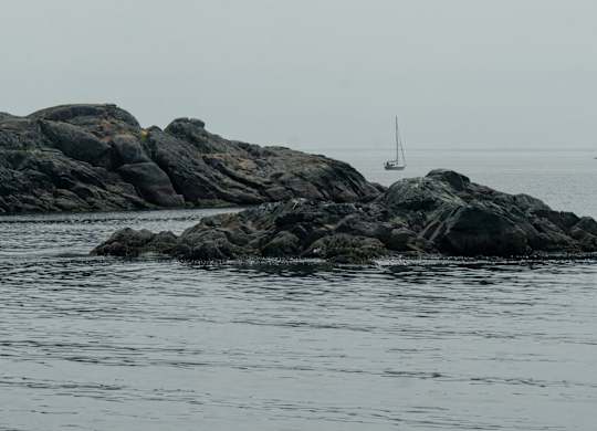 A sailboat is anchored in the distance on a rocky shore.