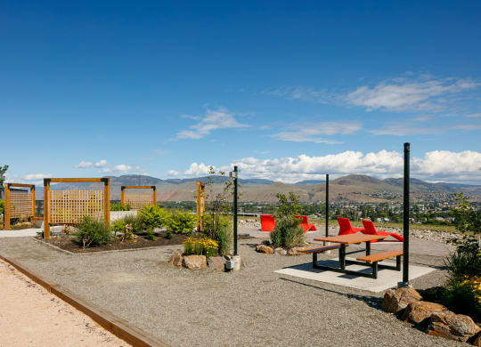 a picnic table and benches sit in a gravel area with a view of the mountains in the