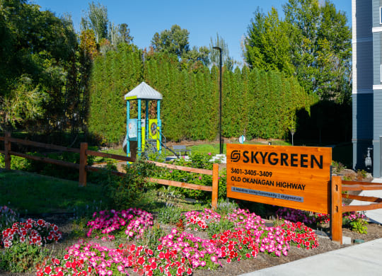 a garden with pink and purple flowers and a blue playground in the background