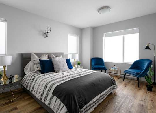 A bedroom with a bed, two chairs, and a lamp.