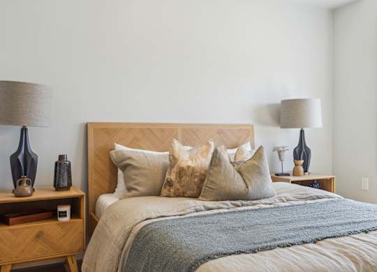 A bed with a wooden headboard and a grey blanket is in the image.