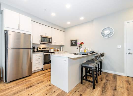 A modern kitchen with a stainless steel refrigerator and a white island with bar stools.