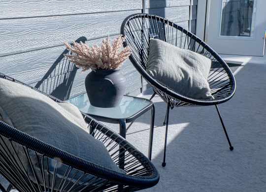Two black wicker chairs with grey cushions are placed on a patio.