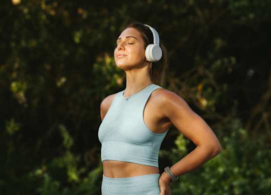 A woman in a blue top and skirt is listening to music with white headphones.