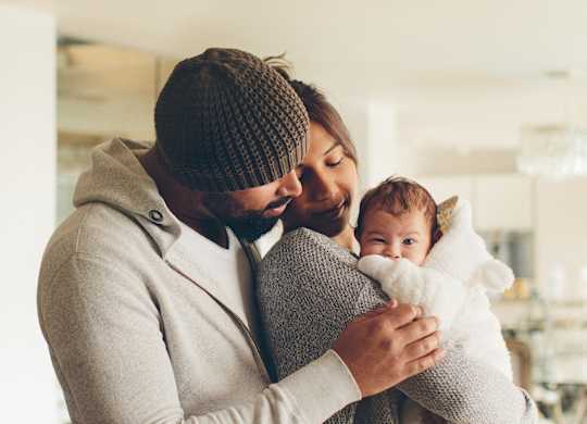 A man in a beanie and a woman in a striped sweater are holding a baby.