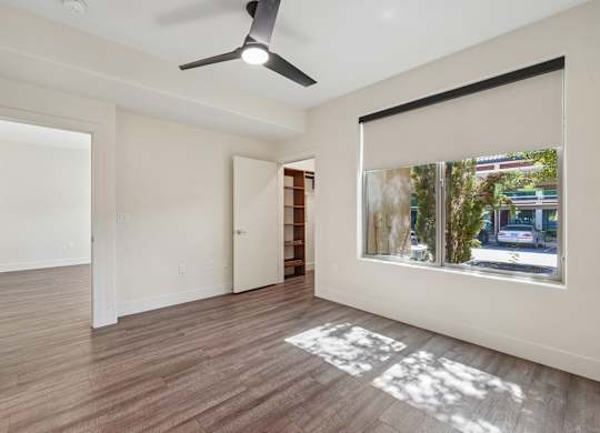 A room with a ceiling fan and a window showing a street view outside.