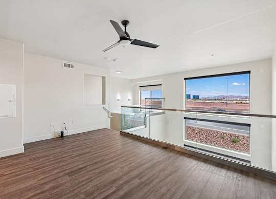 A room with a ceiling fan and a balcony with a view of the outside.