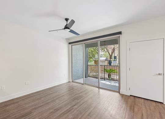 A room with a ceiling fan and sliding glass doors leading to a balcony.