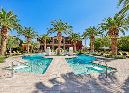 A pool surrounded by palm trees and a building in the background.