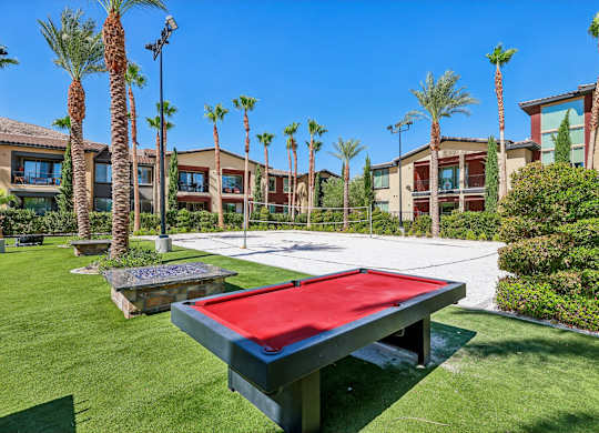A red table tennis table is in the foreground of a photo showing a resort-style outdoor area.