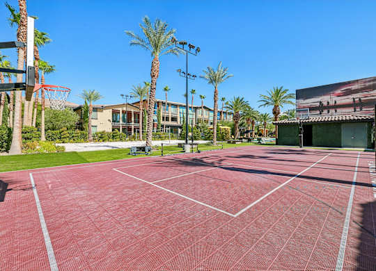 A red tennis court surrounded by palm trees and a building in the background.