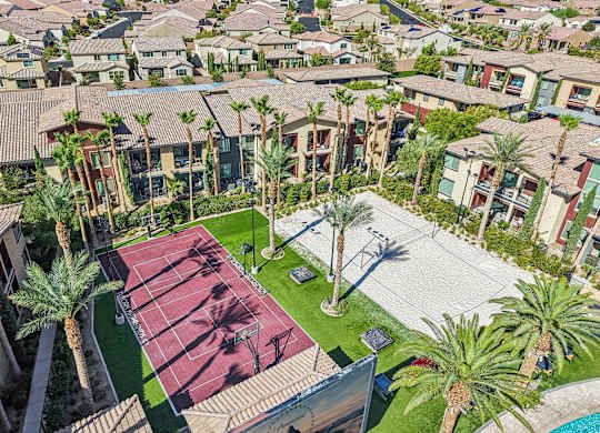 A tennis court is surrounded by palm trees and houses.
