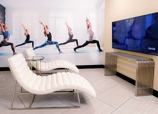 A yoga class is being shown on a television in a room with a white chaise lounge.