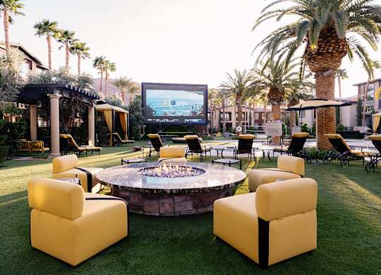 A movie theater is set up outside with yellow chairs and a fire pit.