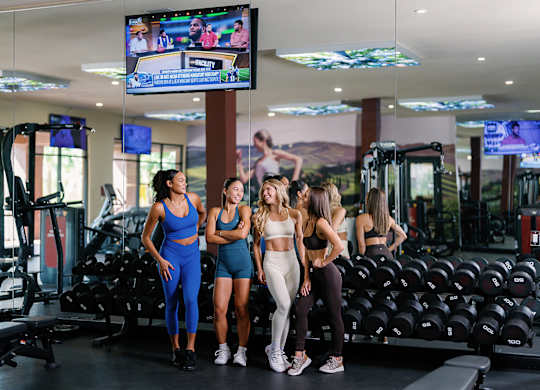 A group of four women are standing in a gym.