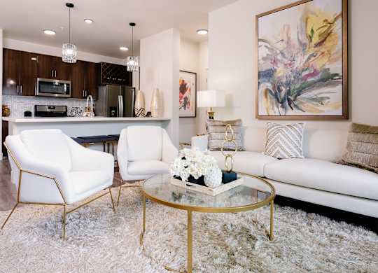 A modern living room with a white sofa, two white chairs, and a glass coffee table.