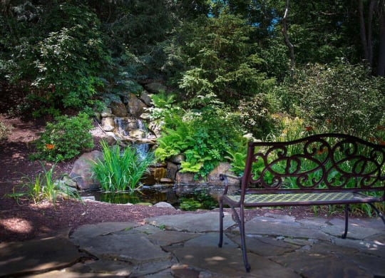 a bench sits on a stone patio next to a pond at Monroeville Apartments, Monroeville, PA