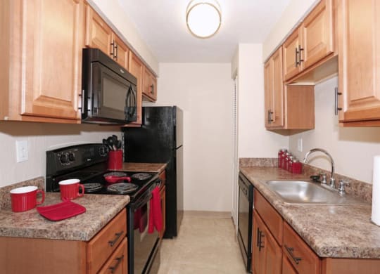 a kitchen with wooden cabinets and black appliances at Monroeville Apartments, Monroeville, Pennslyvania