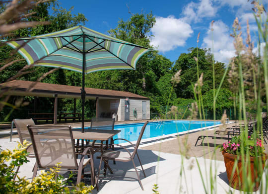 a swimming pool with patio furniture and an umbrella at Monroeville Apartments, Monroeville, Pennslyvania