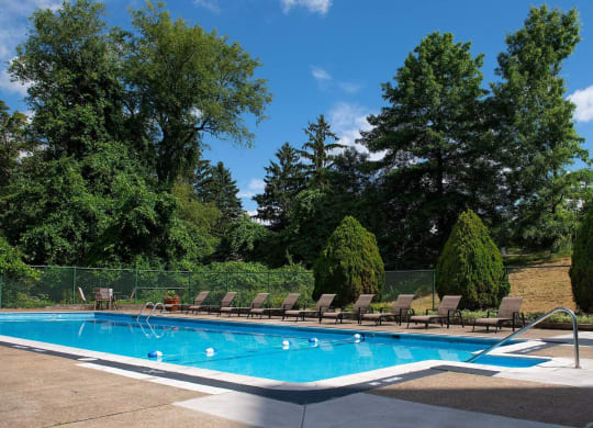 a swimming pool with chaise lounge chairs and trees in the background at Monroeville Apartments, Monroeville, 15146